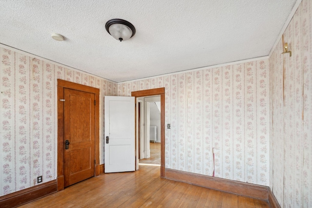 empty room with hardwood / wood-style floors, radiator heating unit, and a textured ceiling