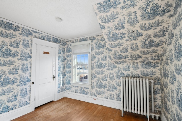 unfurnished room featuring wood-type flooring, radiator, and a textured ceiling