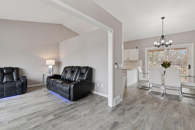 living area with light wood-style flooring, visible vents, baseboards, vaulted ceiling, and an inviting chandelier