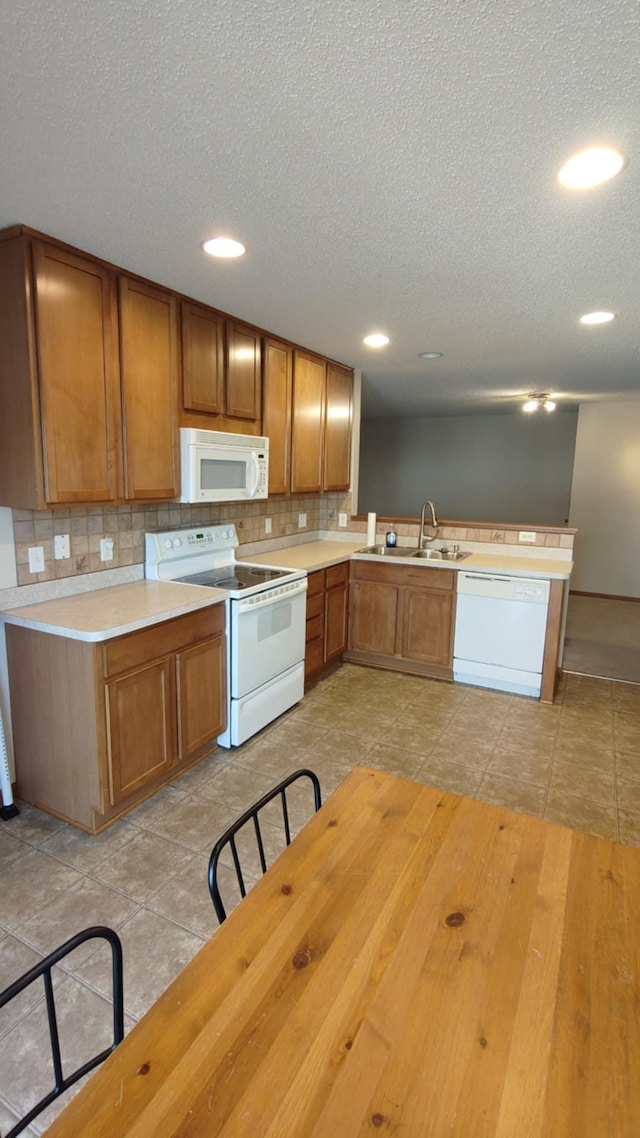 kitchen with white appliances, a sink, a textured ceiling, brown cabinetry, and a peninsula