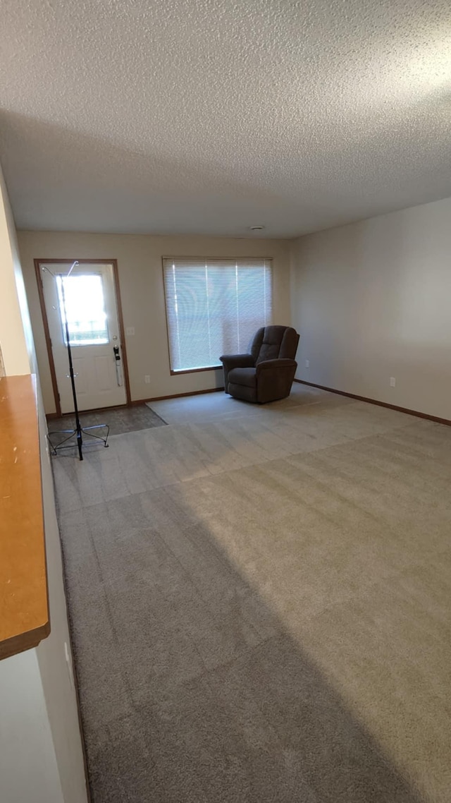 unfurnished room with a textured ceiling, carpet flooring, and baseboards