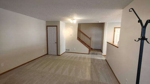 carpeted spare room featuring stairs, a textured ceiling, and baseboards