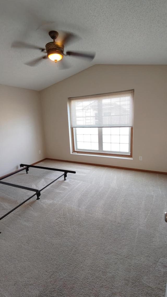 unfurnished room with lofted ceiling, carpet floors, ceiling fan, baseboards, and a textured ceiling