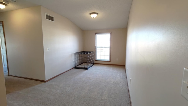 empty room featuring carpet flooring, baseboards, and vaulted ceiling