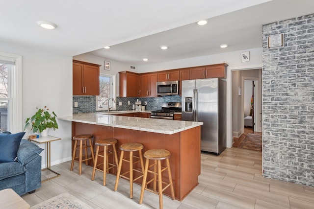 kitchen with appliances with stainless steel finishes, backsplash, light stone countertops, a kitchen bar, and kitchen peninsula