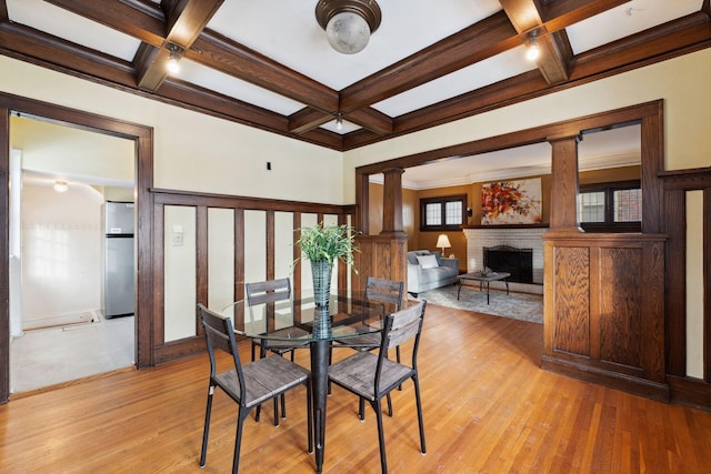 dining room with a fireplace, decorative columns, beamed ceiling, coffered ceiling, and light hardwood / wood-style flooring