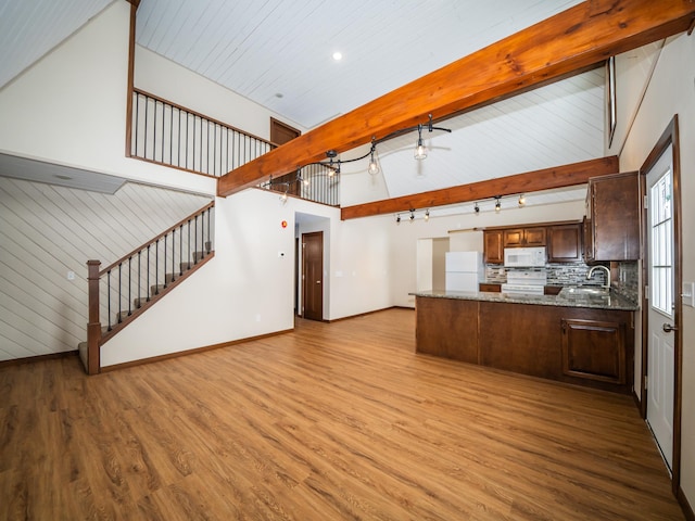 kitchen with sink, white appliances, stone counters, beam ceiling, and light wood-type flooring