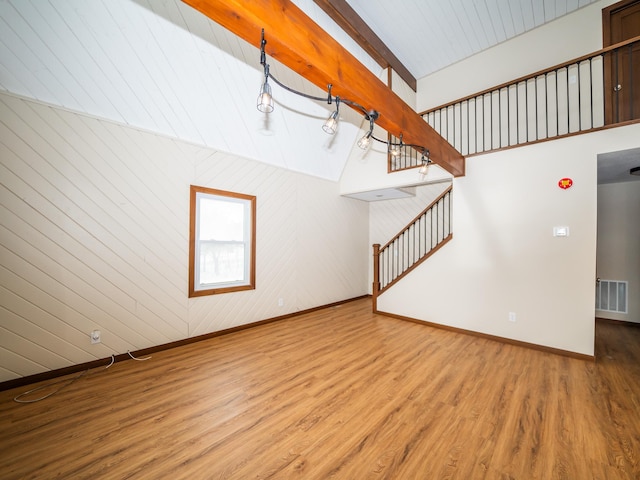 unfurnished living room featuring hardwood / wood-style flooring, wooden walls, and lofted ceiling with beams