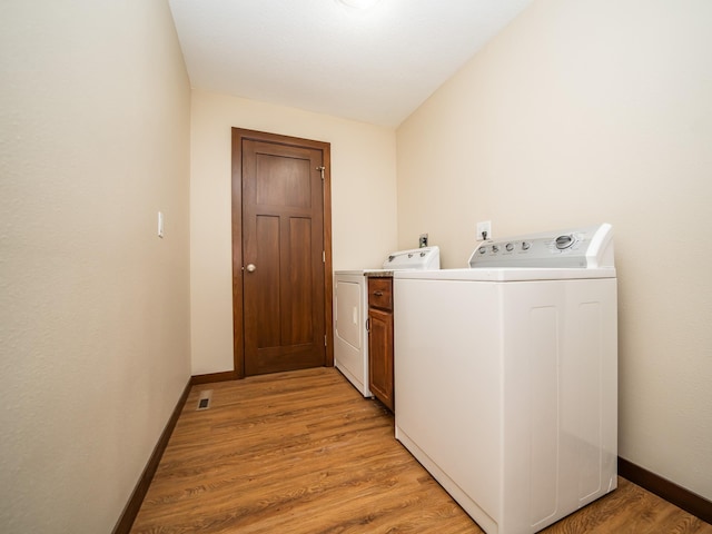 laundry area featuring cabinets, washing machine and dryer, and light hardwood / wood-style flooring