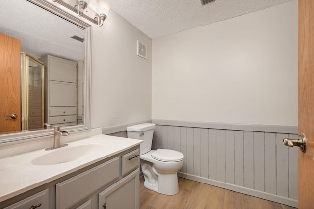 bathroom with toilet, wood walls, wood-type flooring, a textured ceiling, and vanity