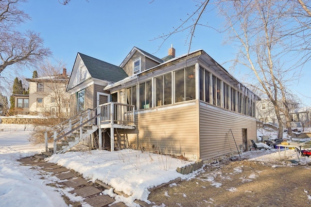 view of snow covered exterior with stairs, a chimney, and a sunroom