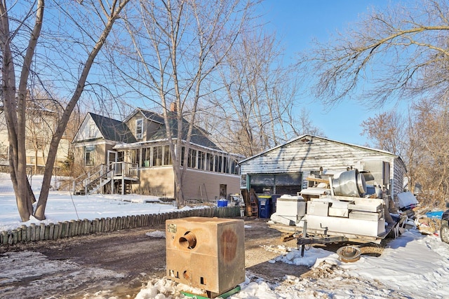 snow covered back of property with a sunroom and fence