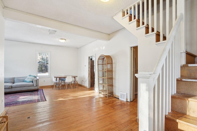 interior space with stairs, a textured ceiling, wood finished floors, and visible vents