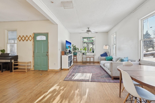 living area with ceiling fan, a textured ceiling, wood finished floors, visible vents, and baseboards