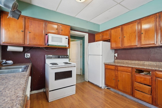 kitchen with a drop ceiling, white appliances, a sink, light countertops, and brown cabinets