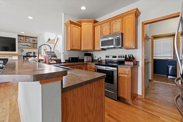 kitchen with stainless steel appliances, a textured ceiling, and light hardwood / wood-style floors