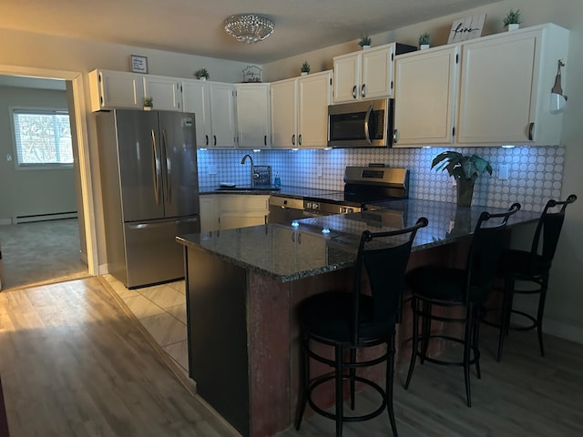 kitchen with appliances with stainless steel finishes, dark stone countertops, white cabinets, a baseboard radiator, and kitchen peninsula