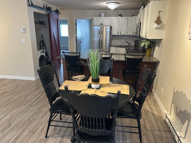 dining space featuring washer / dryer, sink, light wood-type flooring, a baseboard radiator, and a barn door