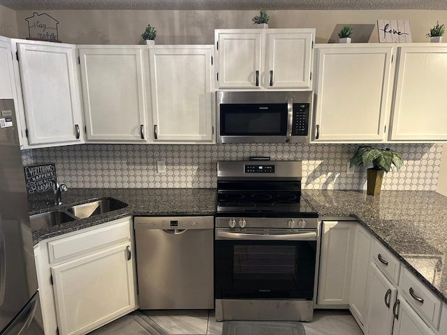 kitchen with dark stone countertops, stainless steel appliances, sink, and white cabinets