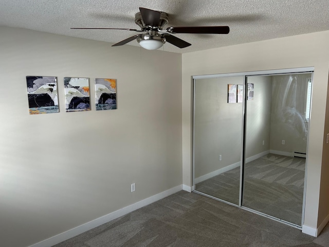 unfurnished bedroom with dark colored carpet, a textured ceiling, baseboard heating, and a closet