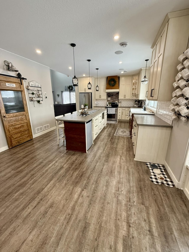 kitchen featuring dark wood-type flooring, decorative light fixtures, a center island, appliances with stainless steel finishes, and backsplash