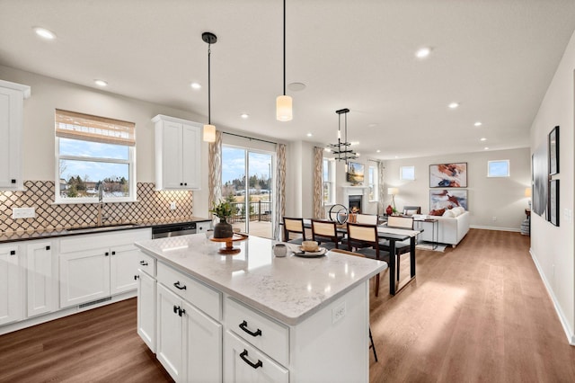 kitchen featuring sink, decorative light fixtures, hardwood / wood-style flooring, a center island, and dark stone countertops