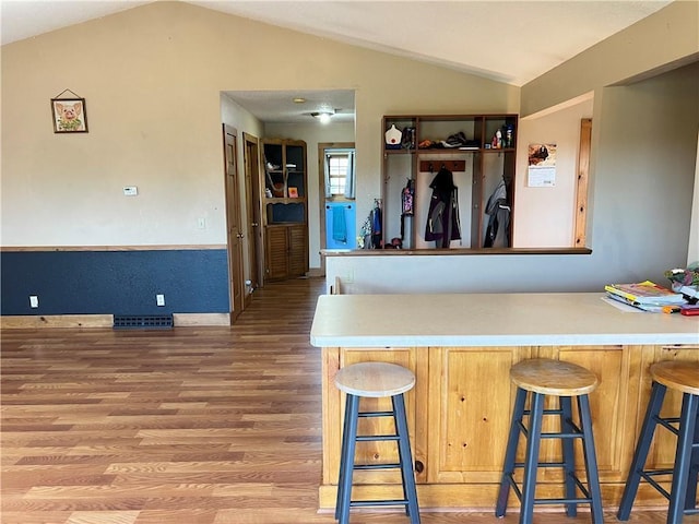 kitchen with wood-type flooring, lofted ceiling, kitchen peninsula, and a breakfast bar area