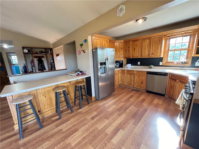 kitchen featuring vaulted ceiling, light hardwood / wood-style flooring, kitchen peninsula, a breakfast bar, and stainless steel appliances