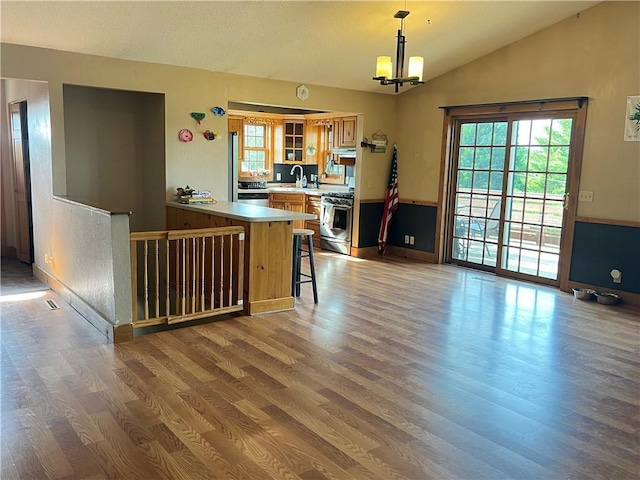 kitchen with kitchen peninsula, pendant lighting, light wood-type flooring, stainless steel range with gas cooktop, and a kitchen bar