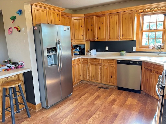 kitchen with light wood-type flooring, a breakfast bar area, and appliances with stainless steel finishes