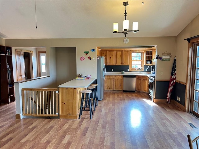 kitchen with appliances with stainless steel finishes, a kitchen bar, hanging light fixtures, kitchen peninsula, and light hardwood / wood-style flooring