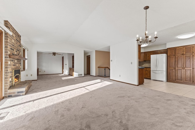 unfurnished living room with vaulted ceiling, a brick fireplace, light colored carpet, and ceiling fan with notable chandelier