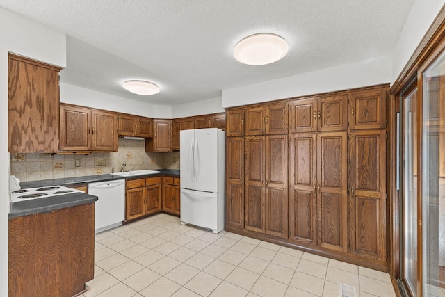 kitchen featuring sink, white appliances, light tile patterned floors, backsplash, and a textured ceiling