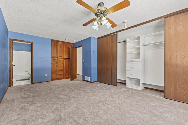 unfurnished bedroom featuring ceiling fan, ensuite bath, light colored carpet, and a textured ceiling