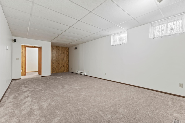 basement with a baseboard radiator, wooden walls, carpet flooring, and a drop ceiling