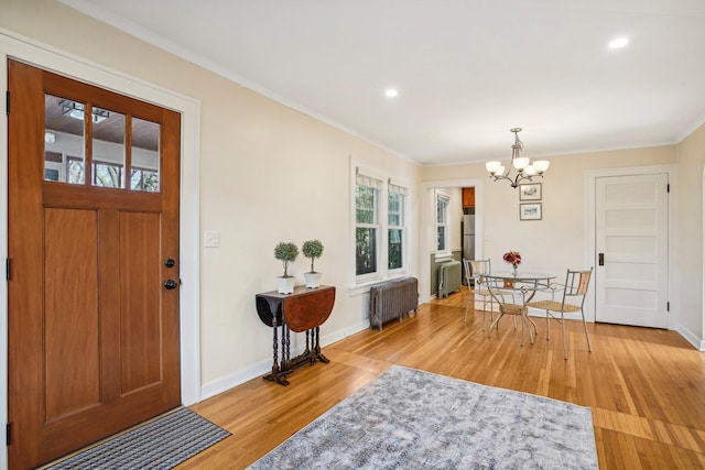 foyer entrance featuring light hardwood / wood-style floors, radiator, crown molding, and an inviting chandelier