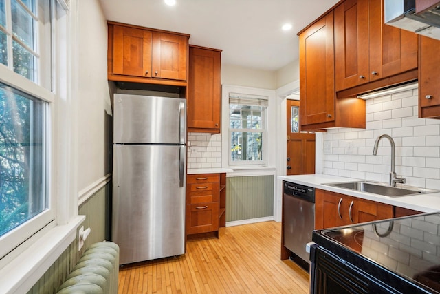 kitchen with sink, appliances with stainless steel finishes, light hardwood / wood-style flooring, and radiator