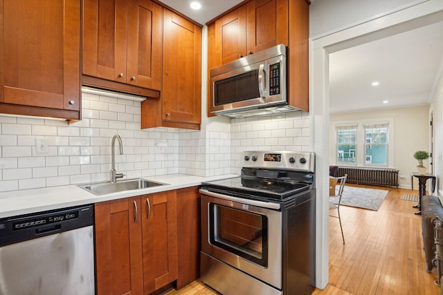 kitchen featuring radiator heating unit, appliances with stainless steel finishes, tasteful backsplash, sink, and light hardwood / wood-style flooring