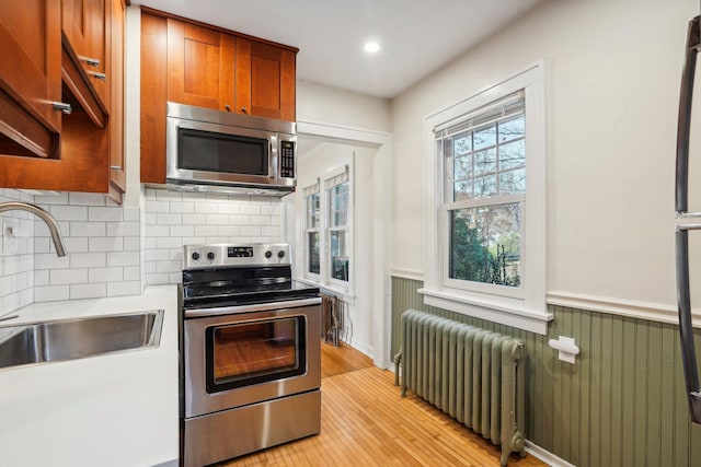 kitchen with radiator, light hardwood / wood-style floors, appliances with stainless steel finishes, sink, and backsplash