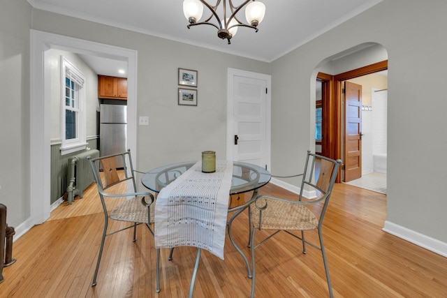 dining space with radiator heating unit, ornamental molding, a notable chandelier, and light wood-type flooring