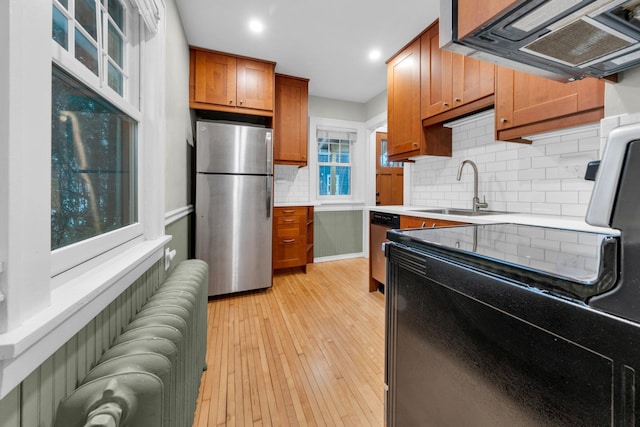 kitchen with sink, light wood-type flooring, radiator, ventilation hood, and stainless steel appliances