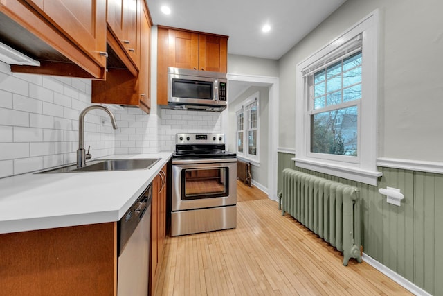 kitchen featuring appliances with stainless steel finishes, radiator, decorative backsplash, sink, and light hardwood / wood-style flooring