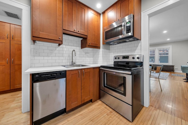 kitchen with sink, backsplash, appliances with stainless steel finishes, and light wood-type flooring