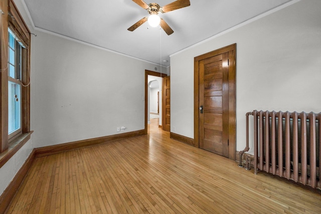 empty room with ceiling fan, radiator heating unit, light hardwood / wood-style flooring, and a wealth of natural light