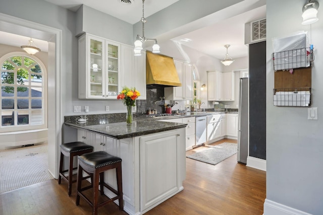 kitchen featuring appliances with stainless steel finishes, pendant lighting, a breakfast bar area, white cabinets, and custom range hood