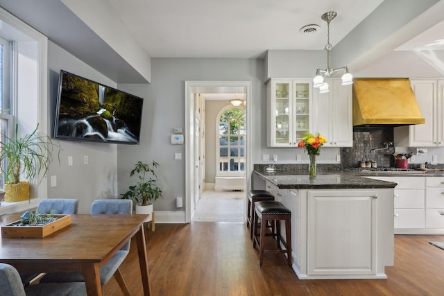 kitchen with white cabinets, a kitchen bar, hanging light fixtures, custom exhaust hood, and dark wood-type flooring