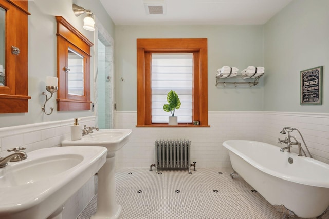 bathroom featuring radiator, a tub, tile walls, double sink, and tile patterned floors