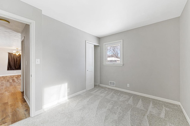 unfurnished bedroom with light carpet, an inviting chandelier, and a closet