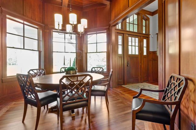 dining area with wooden walls, a chandelier, light hardwood / wood-style flooring, and a wealth of natural light