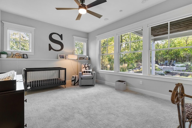 carpeted bedroom with multiple windows, a crib, and ceiling fan